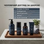 Естетичний квадратний знімок набору чоловічих засобів по догляду за шкірою, включаючи очищувальний гель, зволожувальний крем, засіб після гоління та крем із SPF. Зверху розміщено український текст: 'ЧОЛОВІЧИЙ ДОГЛЯД ЗА ШКІРОЮ' та список 'БАЗОВА РУТИНА' з іконками для очищення, зволоження, захисту та заспокоєння. Стриманий дизайн та м'яке освітлення.